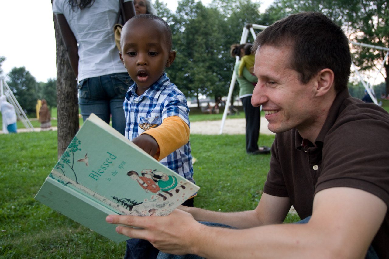 An adult and a delighted young child sharing a picture book outdoors on the grass